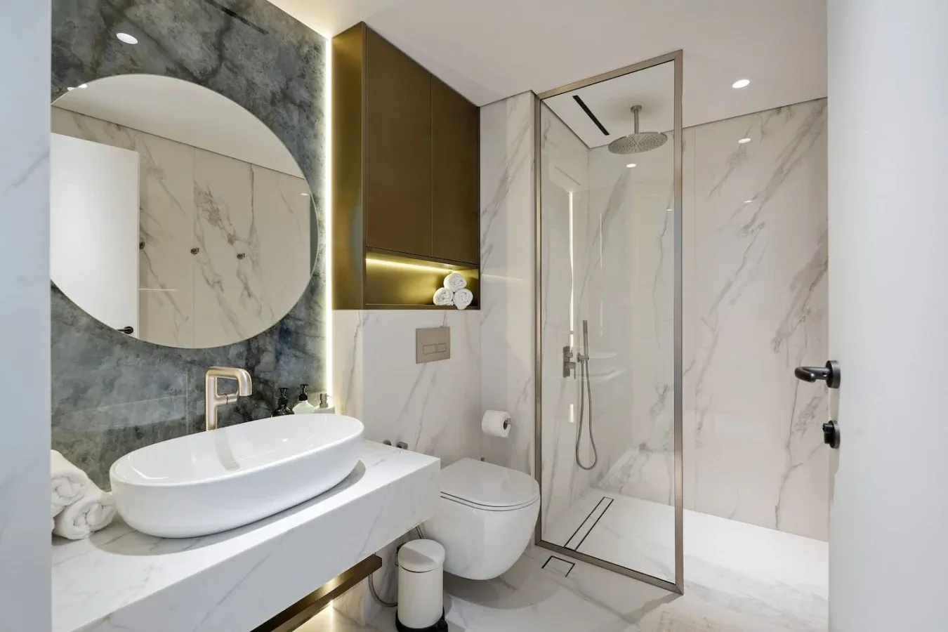 Un baño moderno con tocador, espejo redondo y ducha de vidrio.