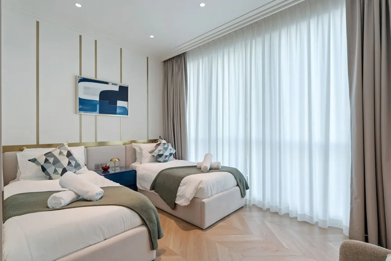 Un dormitorio luminoso con dos camas, cojines estampados y cortinas largas.