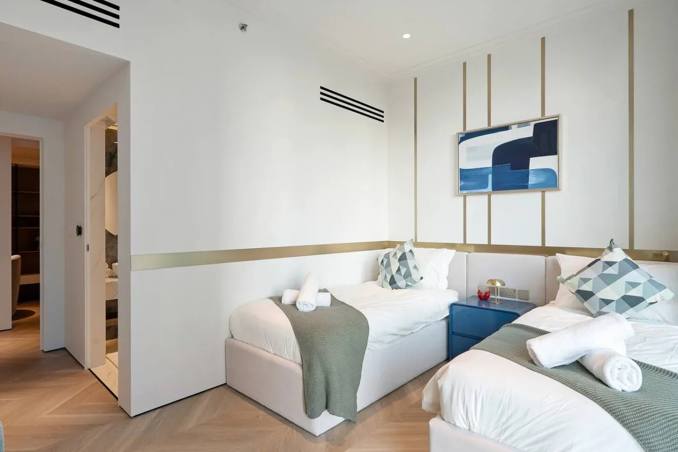 Un dormitorio luminoso con dos camas, cojines estampados y arte abstracto en la pared.