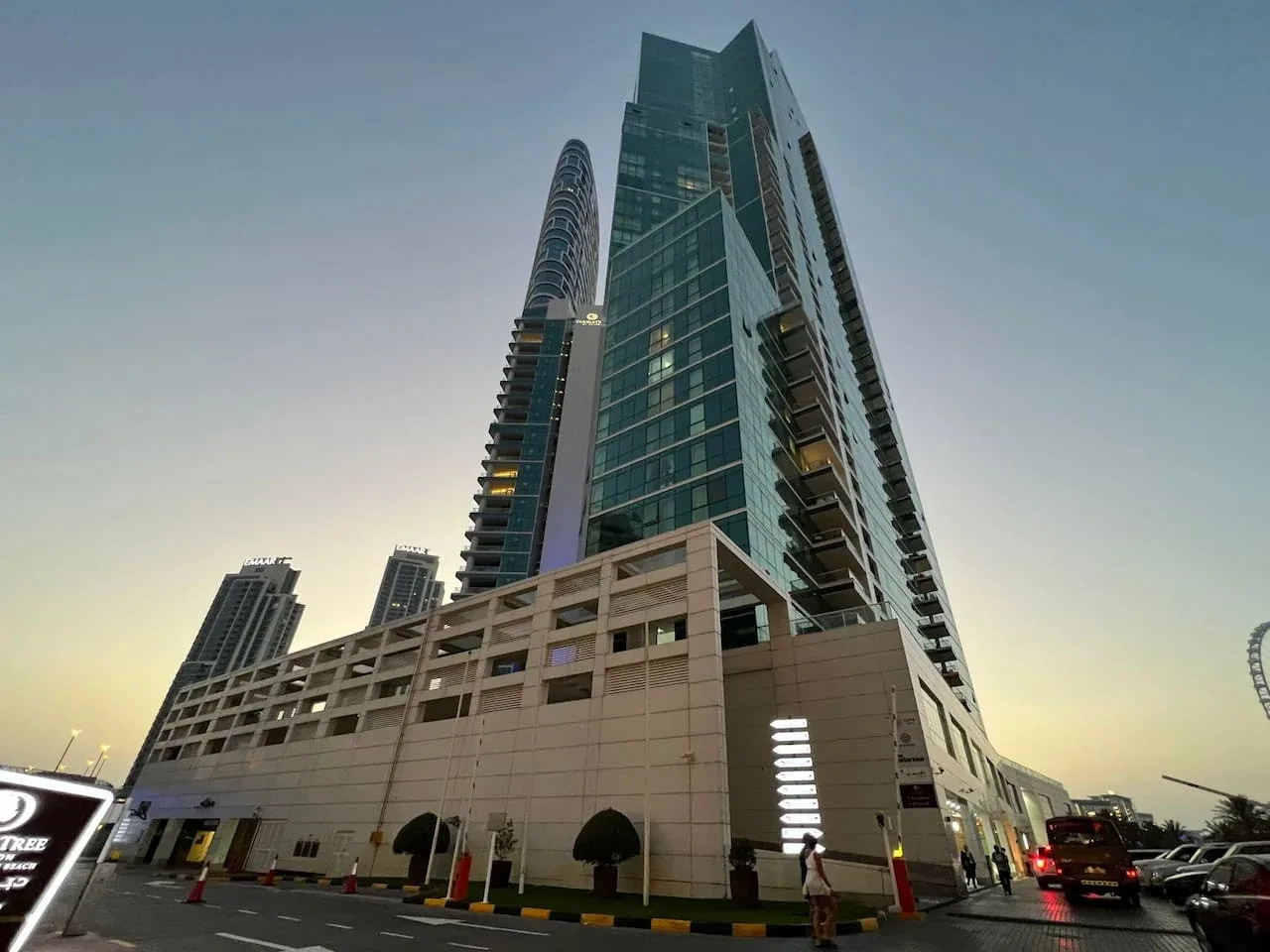 Un moderno edificio alto se eleva sobre una estructura comercial más baja al anochecer.