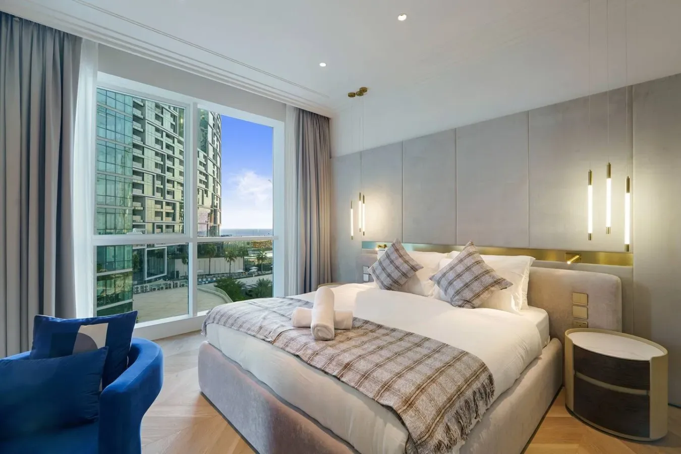 Un dormitorio con una cama grande, ropa de cama a cuadros y una ventana con vista a edificios cercanos.