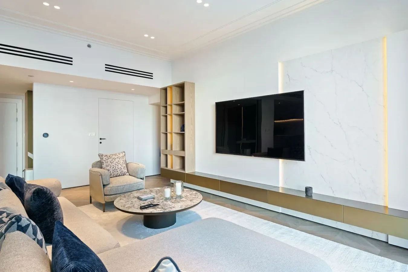 Una sala de estar luminosa con asientos, una mesa de centro redonda y un televisor en la pared.