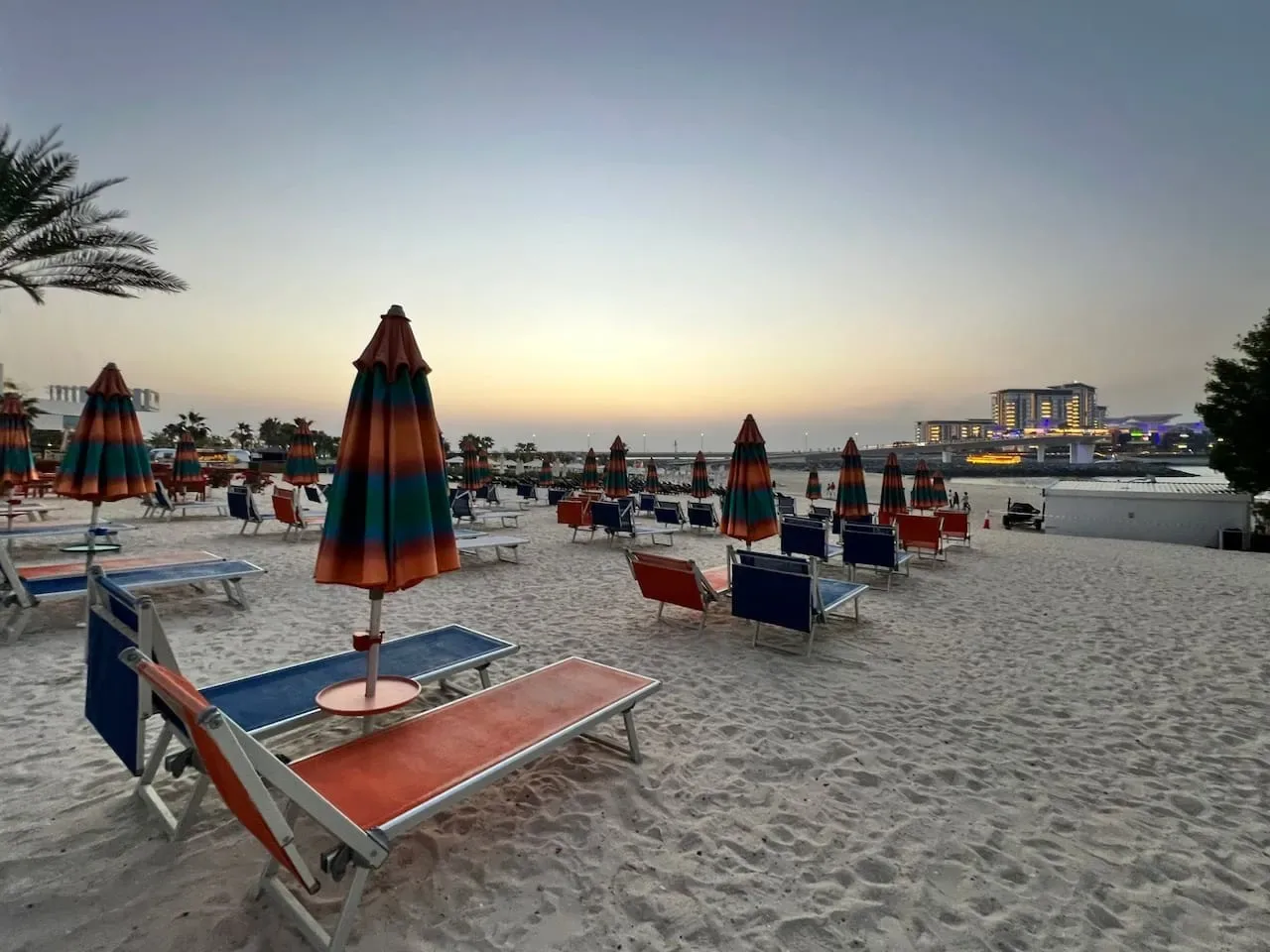 Una zona de playa con asientos y sombrillas coloridas cerradas al atardecer.