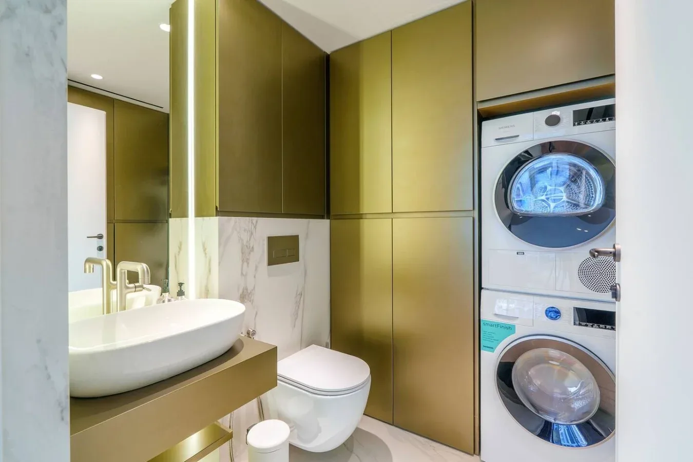 Un baño moderno con lavabo, inodoro y máquinas de lavado apiladas.