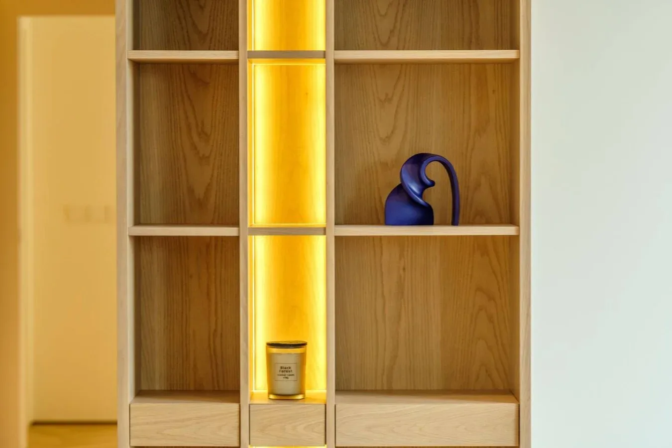 Una estantería de madera con una sección estrecha iluminada y objetos decorativos.