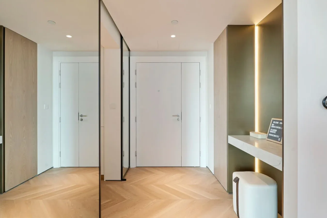 Una entrada moderna y luminosa con puertas blancas, suelo de madera y un estante empotrado.