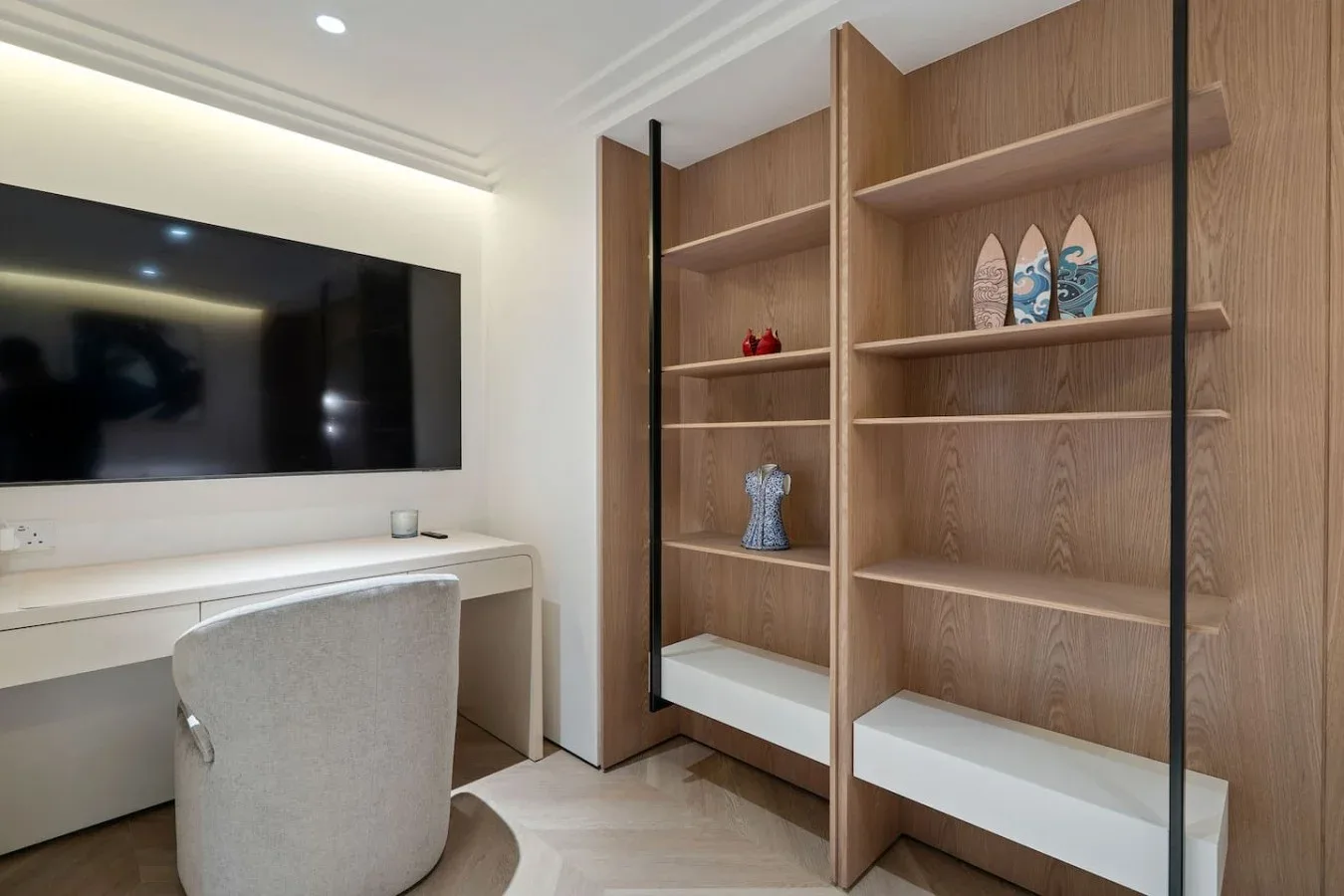 Una habitación luminosa cuenta con un televisor montado en la pared, un escritorio y estantes abiertos de madera.
