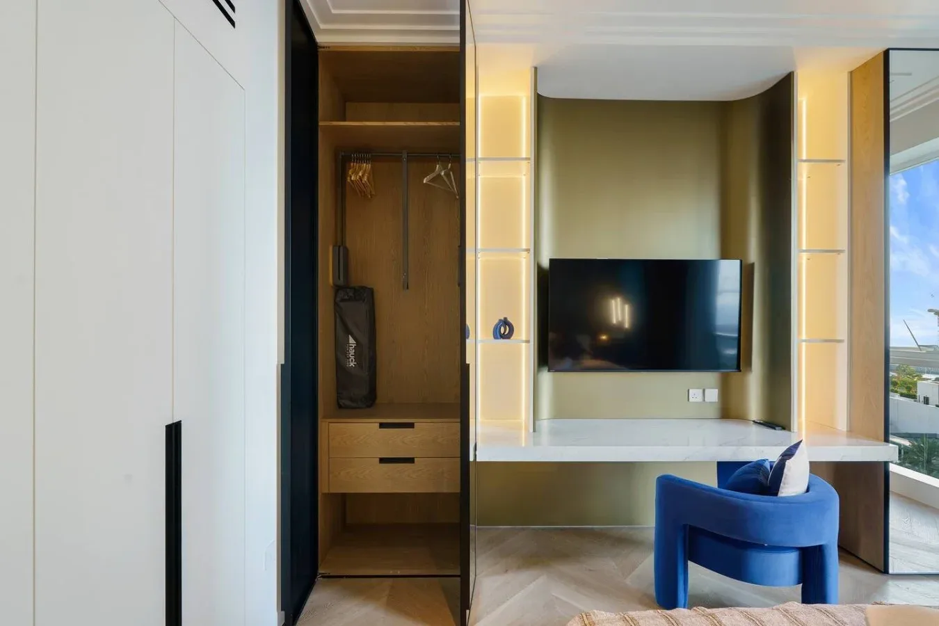 Una habitación moderna tiene un televisor en la pared, estantes empotrados y una silla azul.
