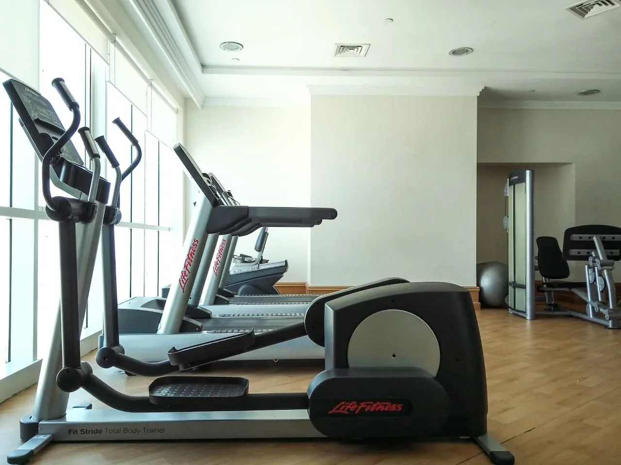 Un gimnasio luminoso con máquinas de ejercicio junto a grandes ventanas.
