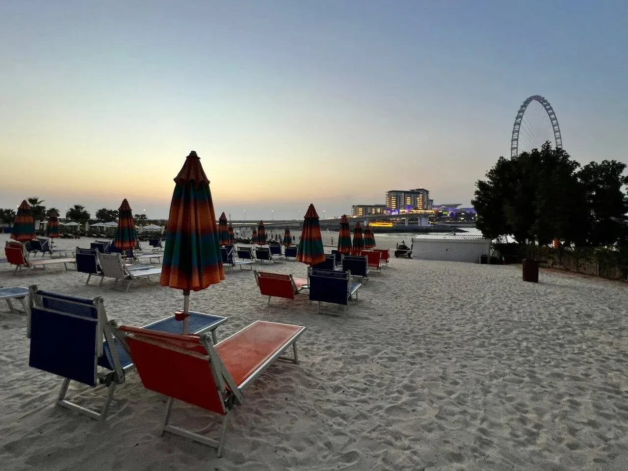 Una playa de arena al atardecer, con tumbonas y sombrillas cerradas.