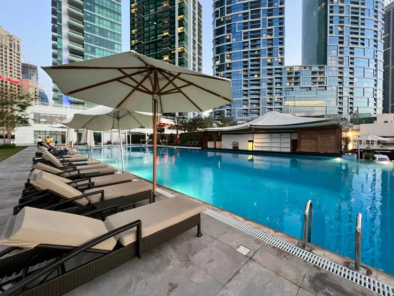 Una piscina al aire libre con asientos y sombrillas, rodeada de edificios altos.