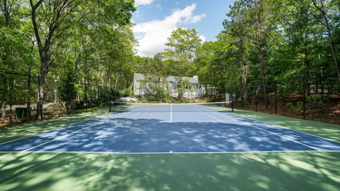 A tennis court surrounded by leafy trees.