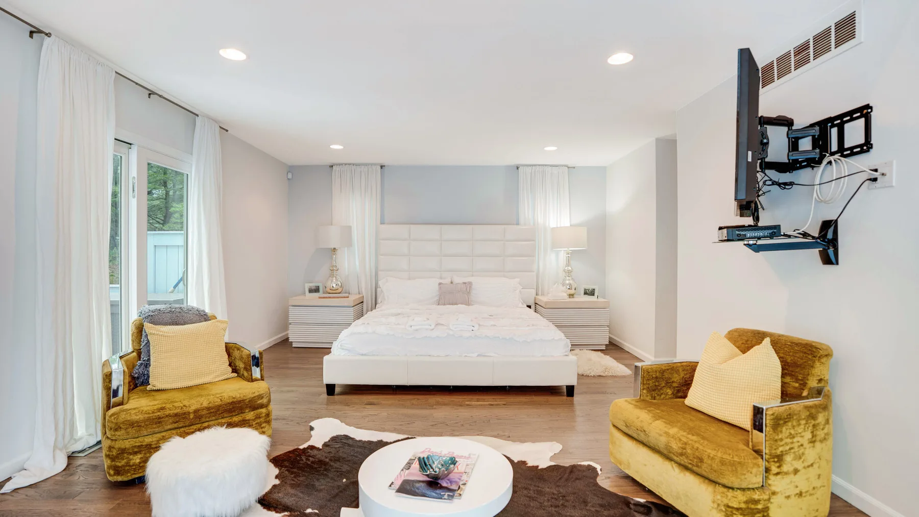 A bright bedroom with a large bed, matching bedside tables, and two upholstered seats.