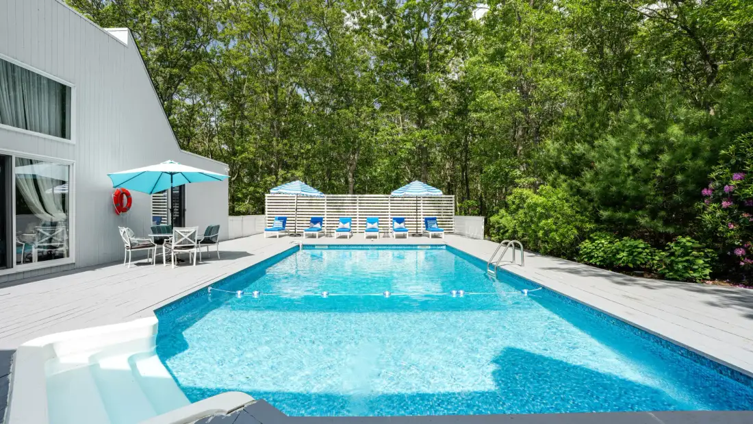 Outdoor swimming pool beside a white building, with lounge seating and trees.