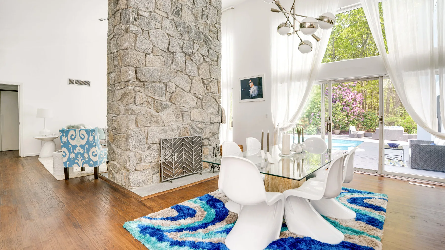 A bright dining area with a glass table beside a large stone fireplace.