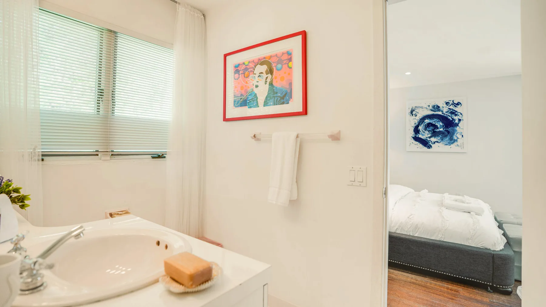 A bright bathroom with a bathtub beside a bedroom.