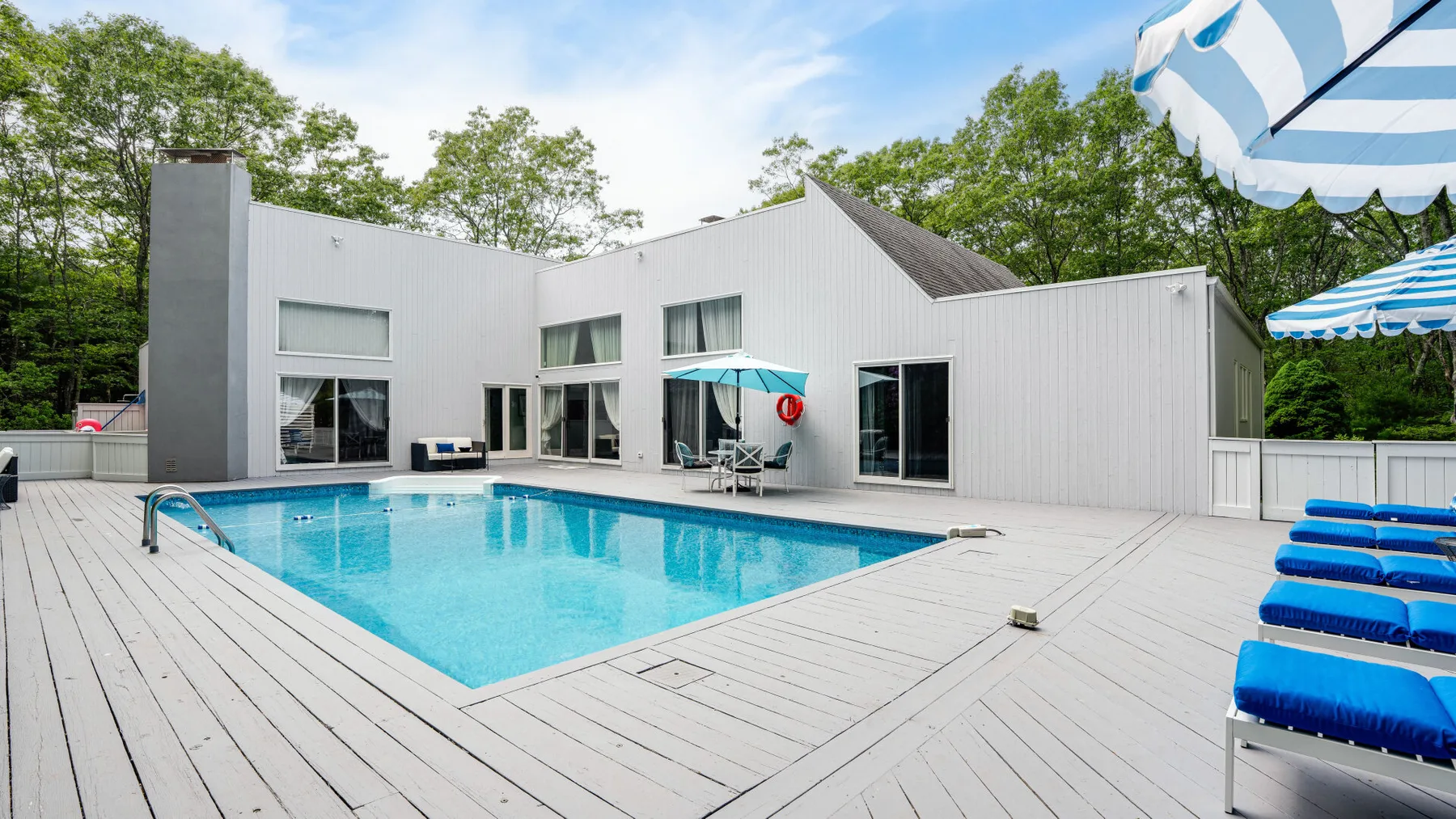 A swimming pool sits beside a modern white building with a broad deck.
