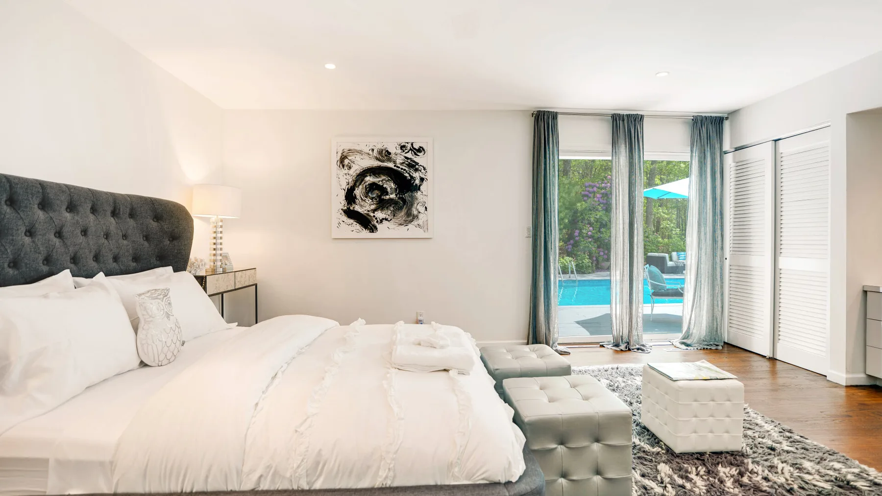 A bright bedroom with a large bed and sliding glass doors opening to a pool view.