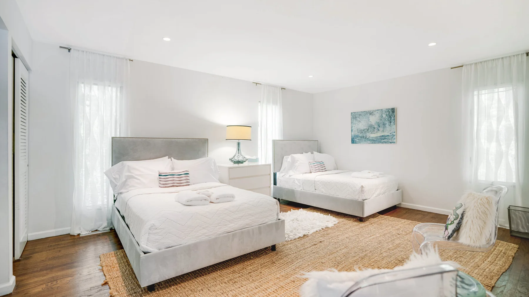 A bright bedroom with two beds, white bedding, and a woven rug.