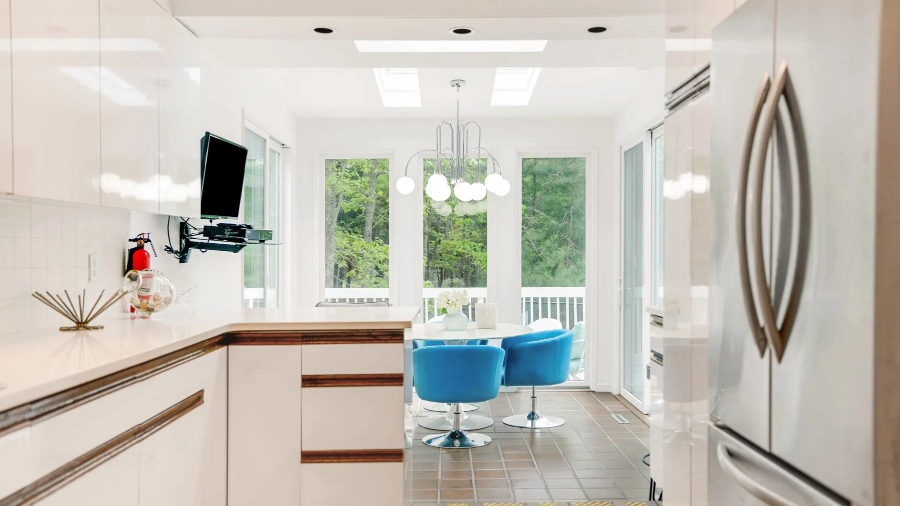 A bright kitchen opens onto a dining area with blue seating and large windows.