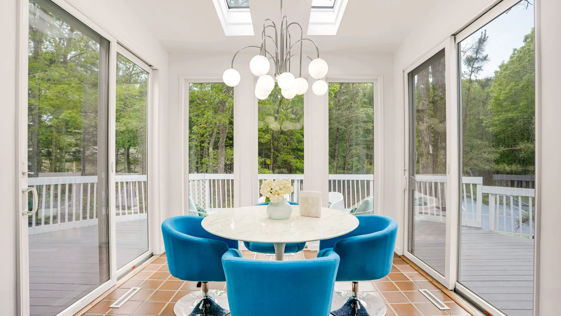 A bright glass-walled dining area with an oval table and blue seating.
