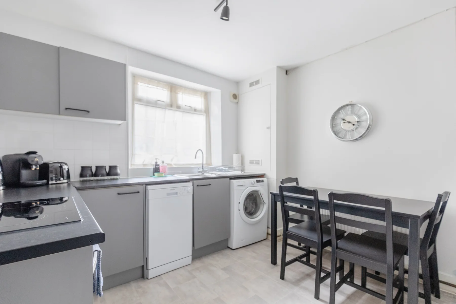 A bright kitchen with gray cabinets, appliances, and a dining table.