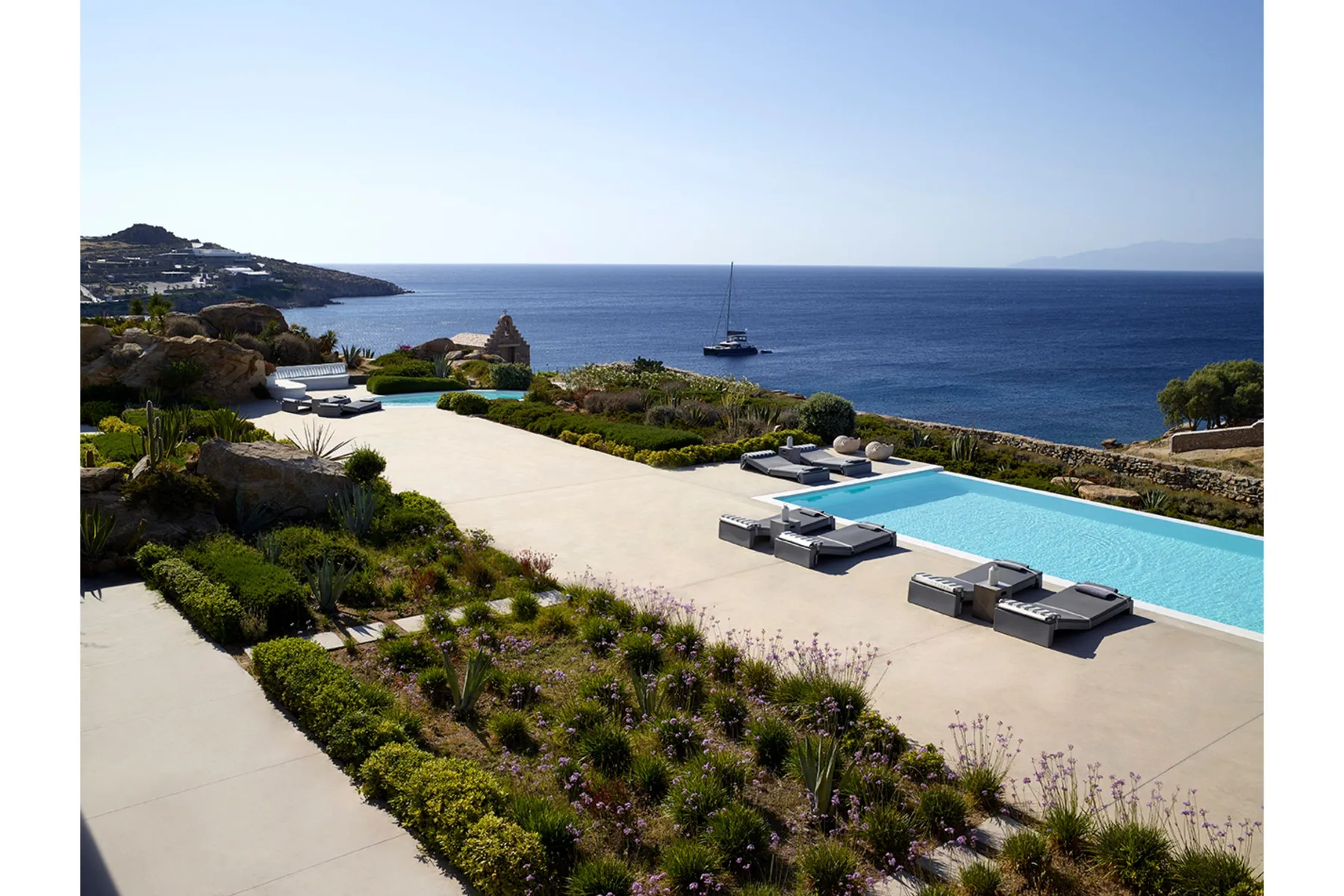 A seaside terrace has a swimming pool, lounge seating, and views of the sea.
