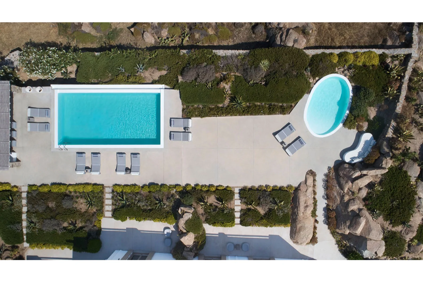 An aerial view shows a rectangular swimming pool and a smaller curved pool on a landscaped patio.