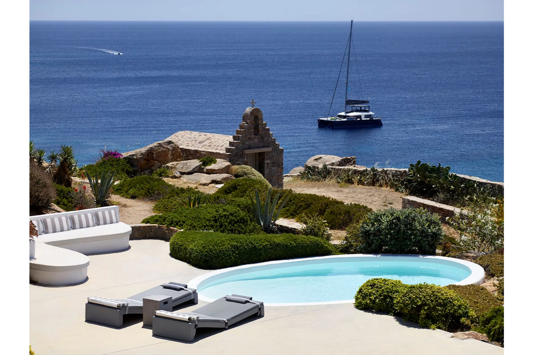 A seaside terrace features a swimming pool, lounge seating, and views of the ocean.