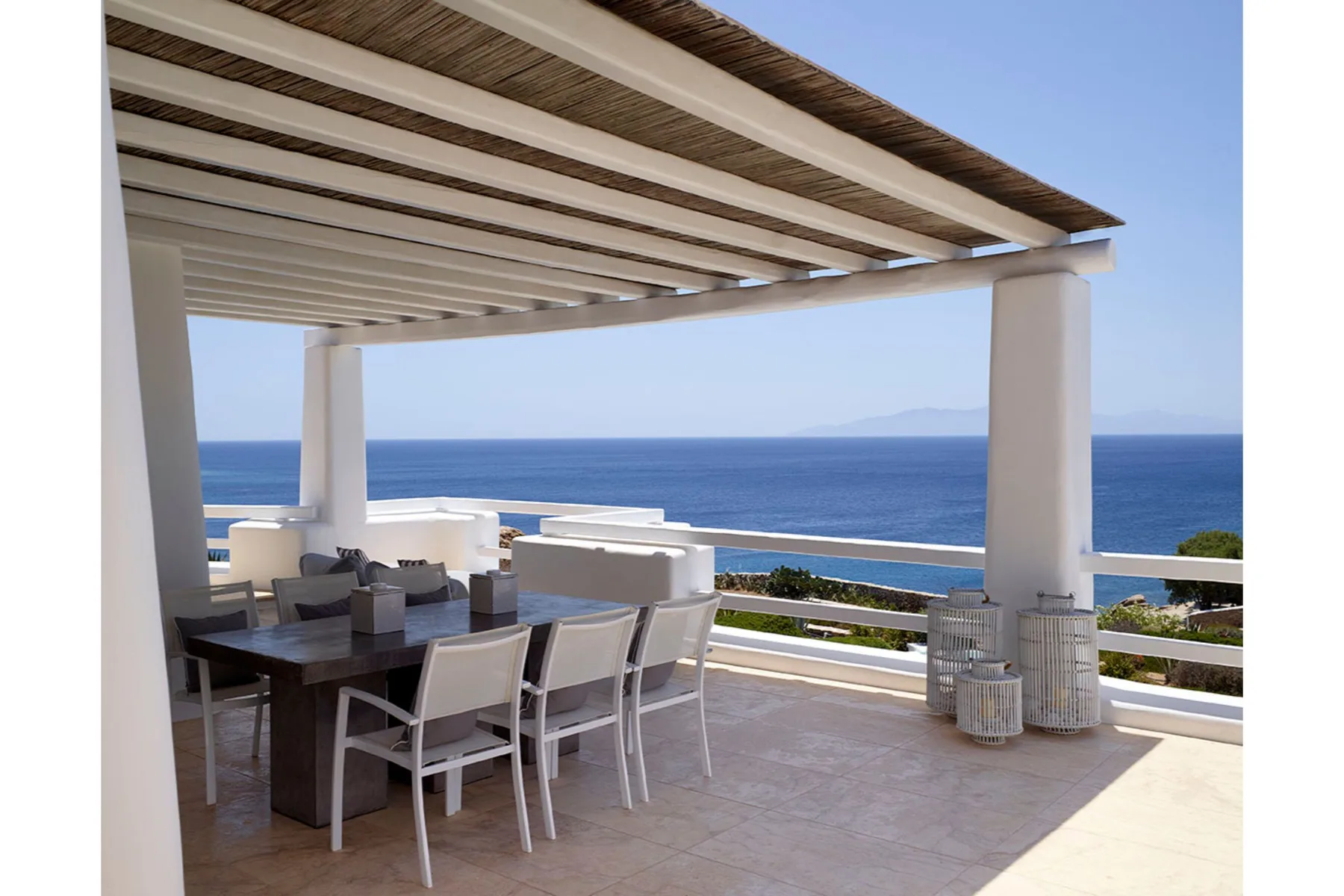 A shaded outdoor dining area with seating overlooks the ocean.