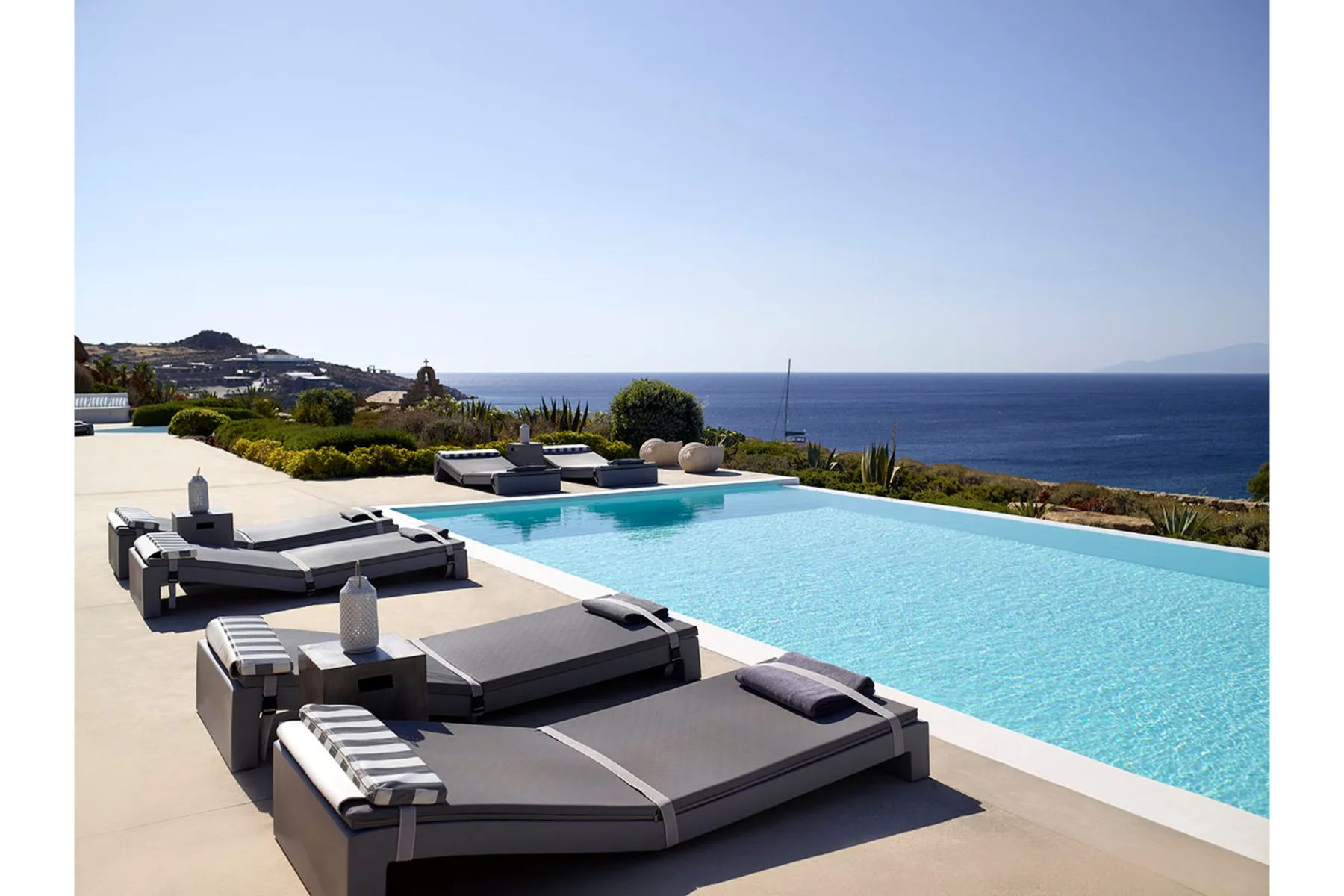 An outdoor poolside terrace overlooks the sea, with lounge seating beside the water.