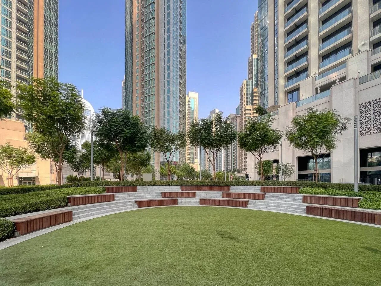 Un patio ajardinado con césped verde, asientos curvos y árboles alrededor.