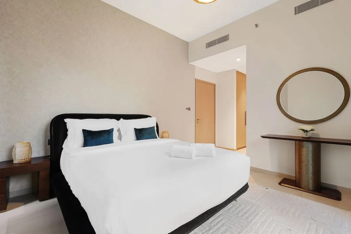 Un dormitorio luminoso con una cama bien tendida y un espejo ovalado en la pared.