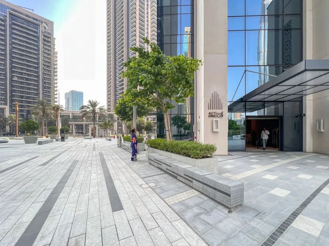 Un edificio moderno con fachada de vidrio da a una amplia plaza pavimentada con árboles.