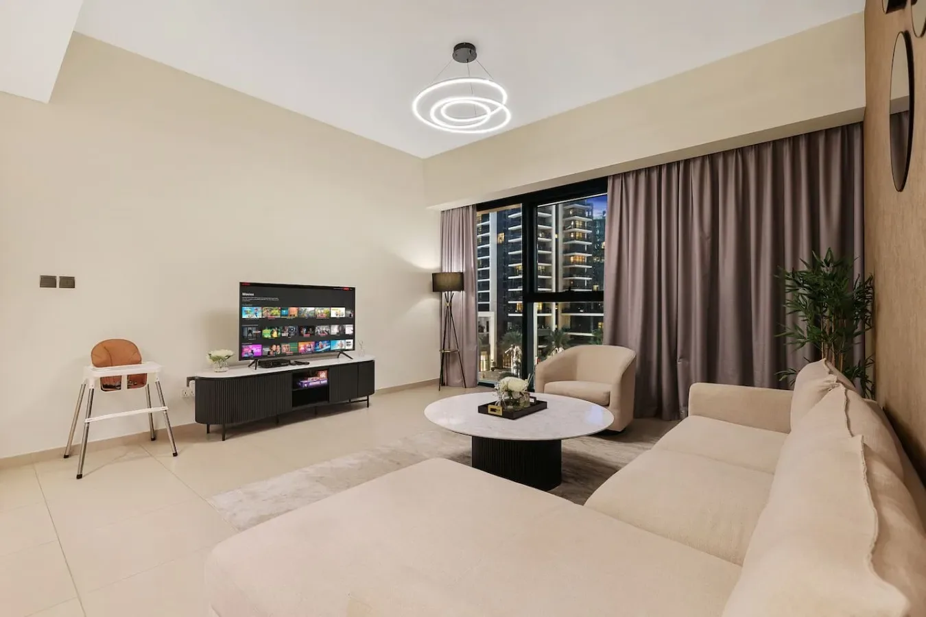 Una sala de estar con asientos, un televisor y grandes ventanas con cortinas.