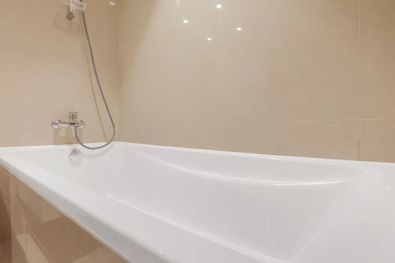 Una bañera con ducha de pared frente a paredes de azulejos beige.