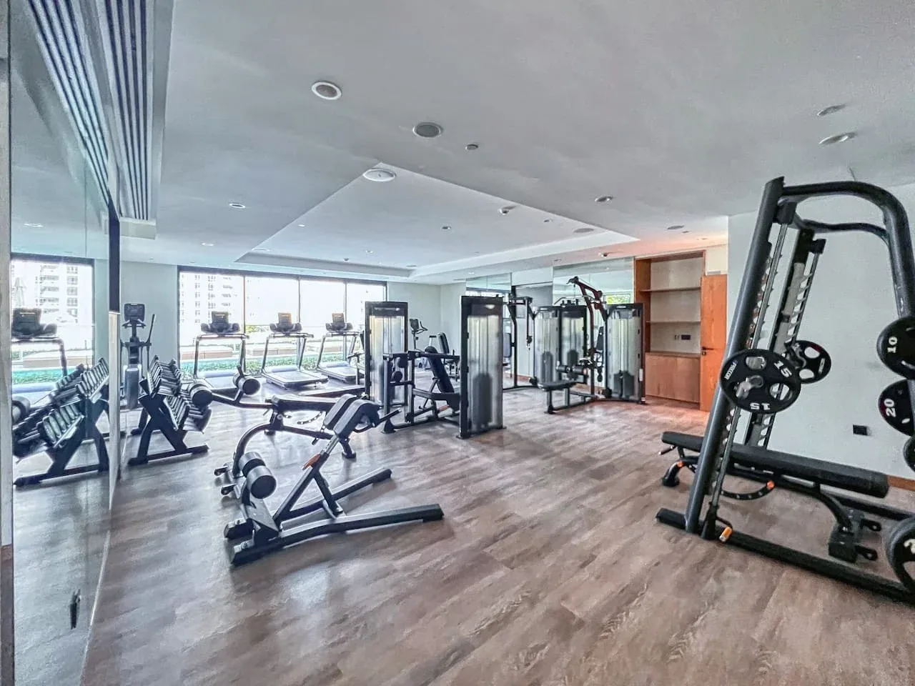 Un gimnasio amplio con máquinas de ejercicio y grandes ventanas a lo largo de una pared.