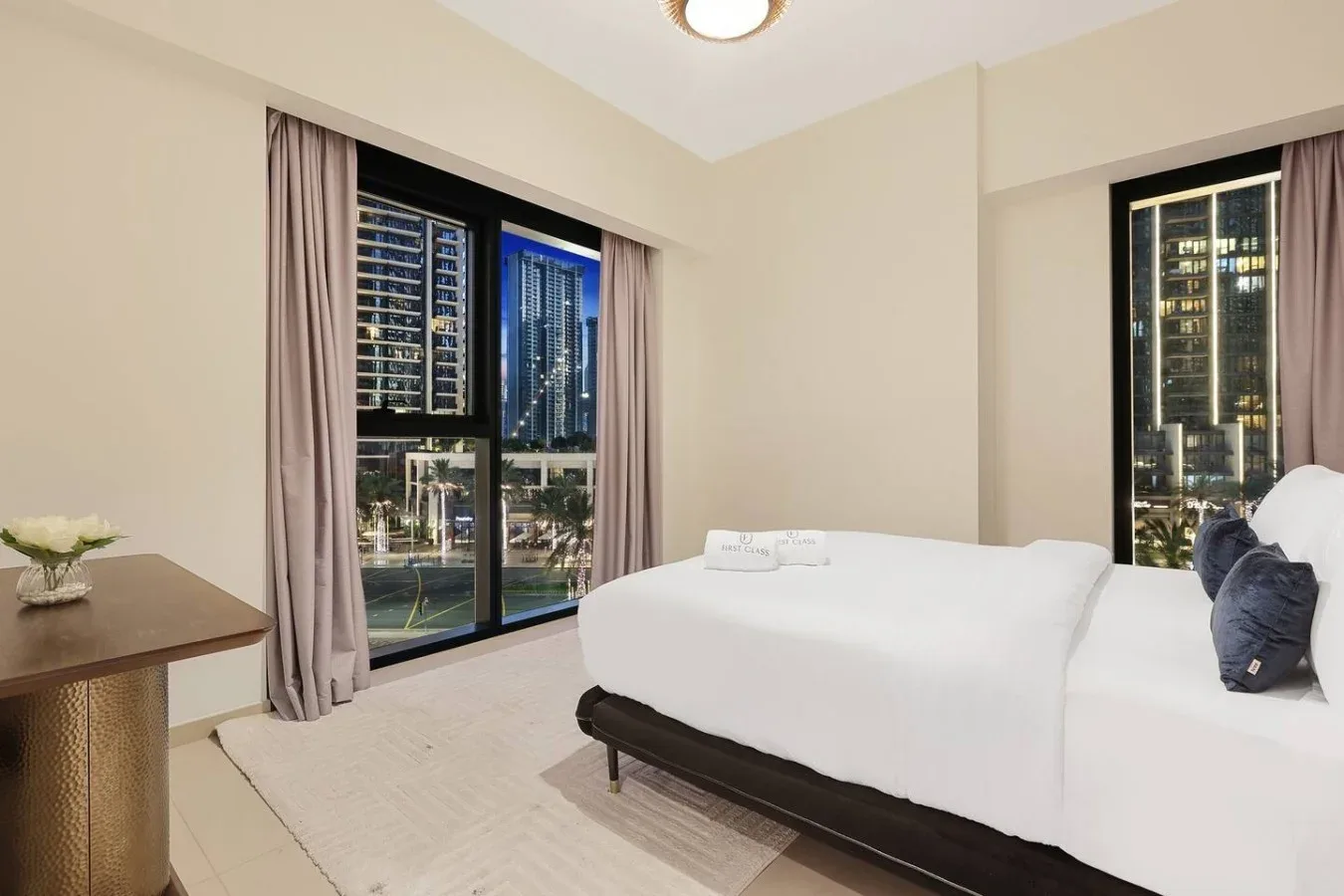 Un dormitorio con una cama grande junto a ventanales con vistas a edificios de la ciudad.