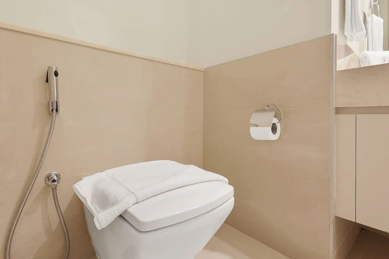 Un baño con un inodoro suspendido y una ducha higiénica de mano.