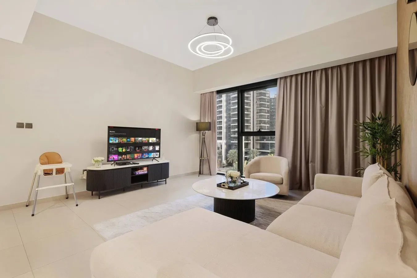 Una sala de estar luminosa con asientos claros, una mesa de centro y un televisor.