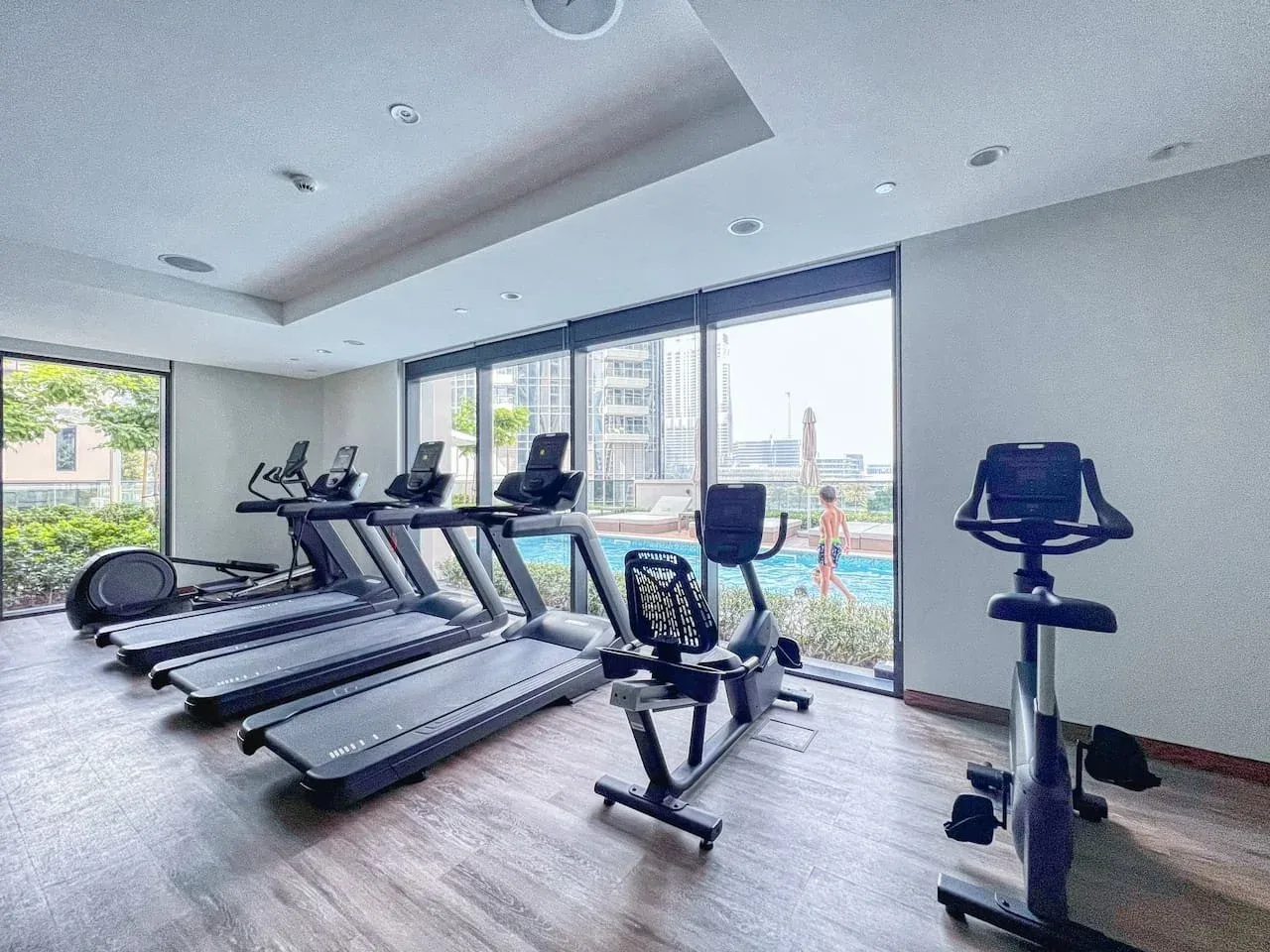 Un gimnasio con cintas de correr y bicicletas estáticas junto a grandes ventanales.