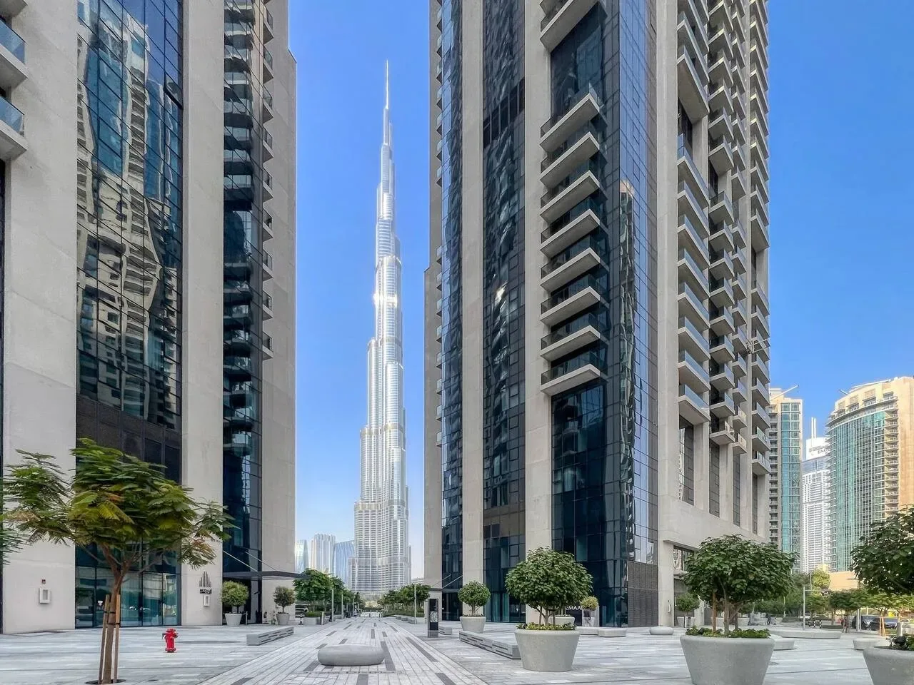 Una plaza urbana entre edificios altos, con un rascacielos esbelto al fondo.