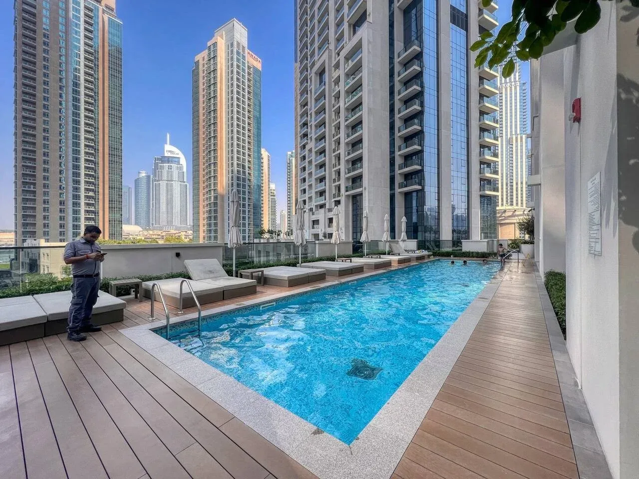 Una piscina en la azotea está rodeada de edificios altos, con una terraza de madera al lado.