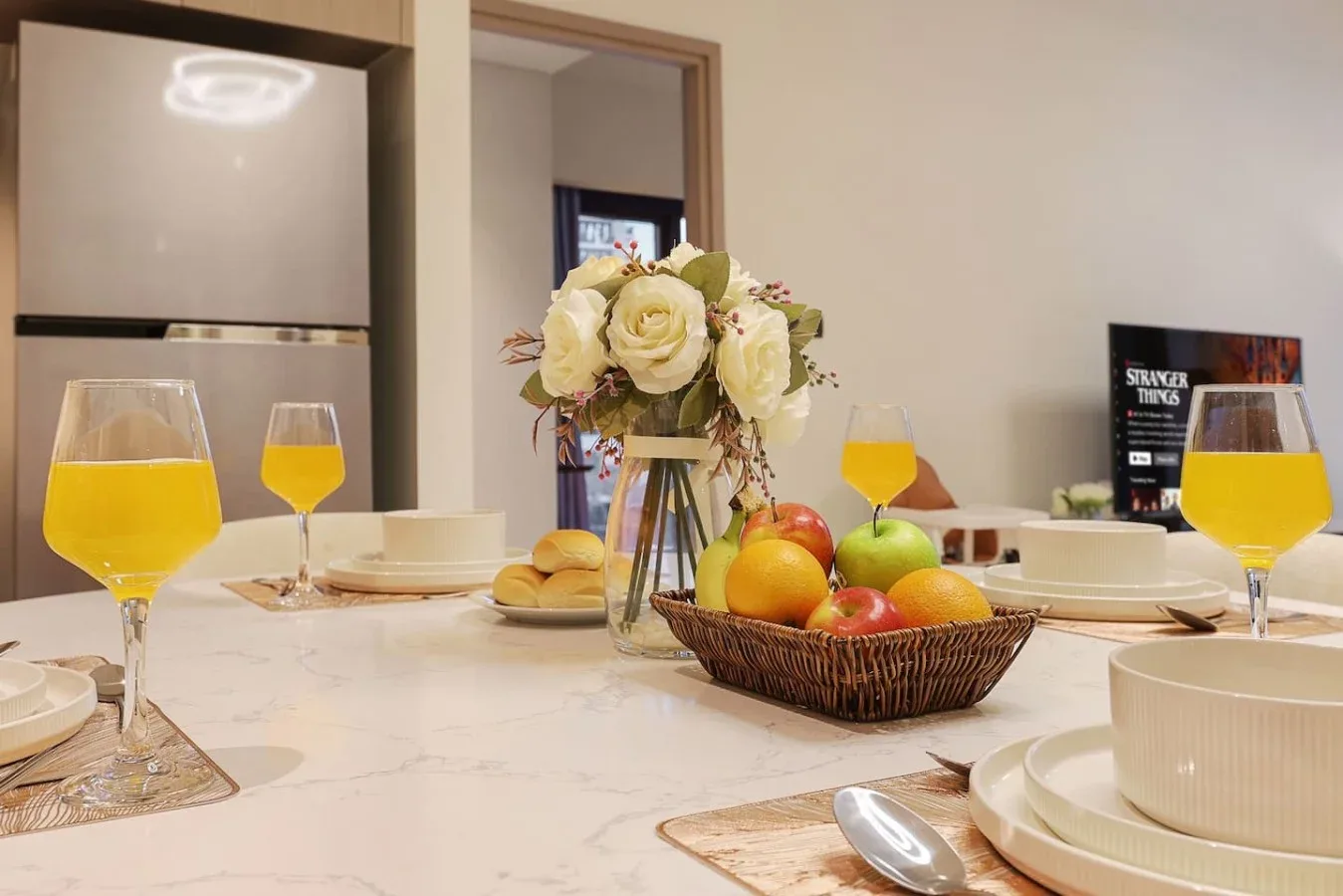 Una mesa de comedor con platos, fruta, flores y vasos de jugo de naranja.