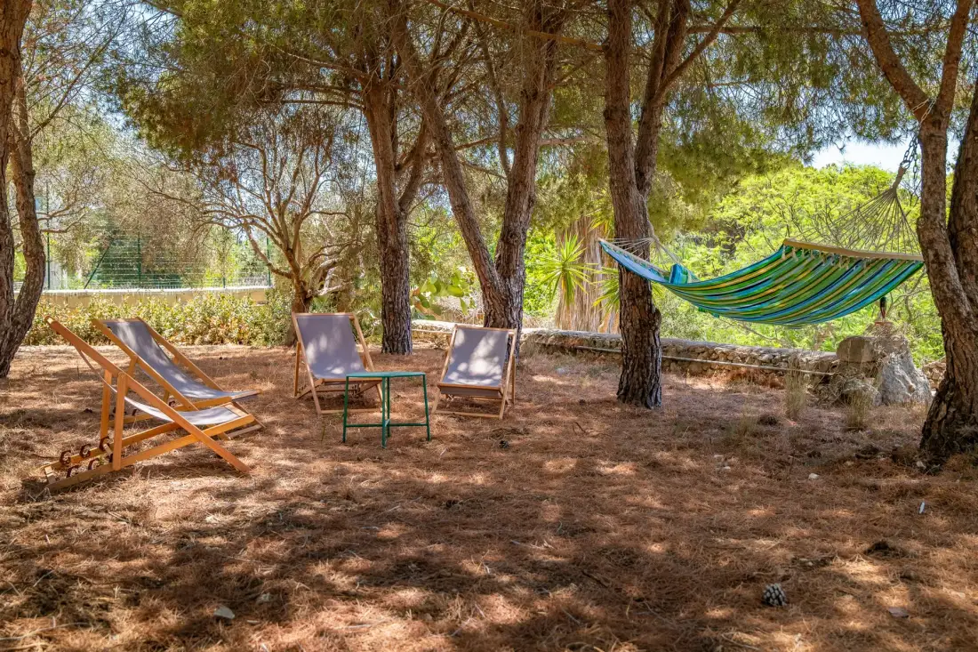 Zona de estar al aire libre a la sombra de árboles, con una hamaca y sillas.