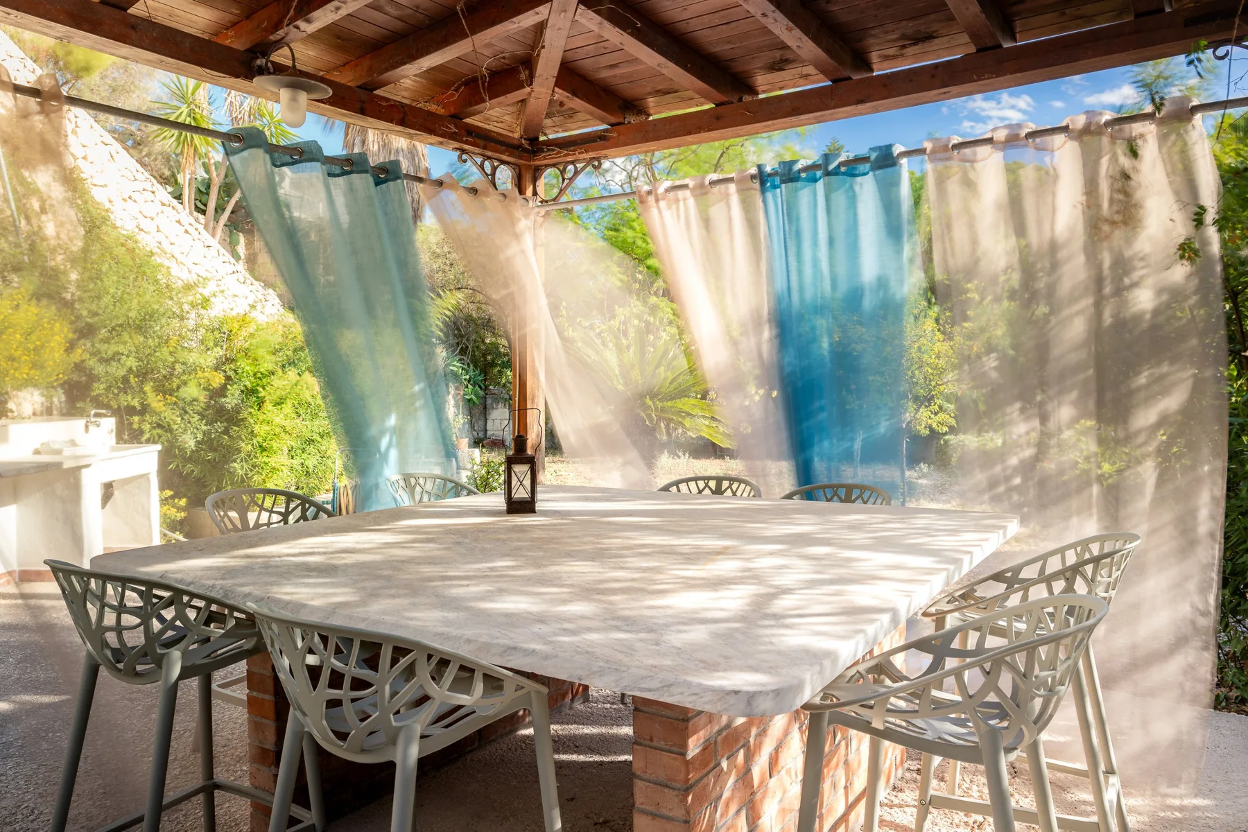 Una zona de comedor al aire libre con mesa y asientos bajo una cubierta de madera.