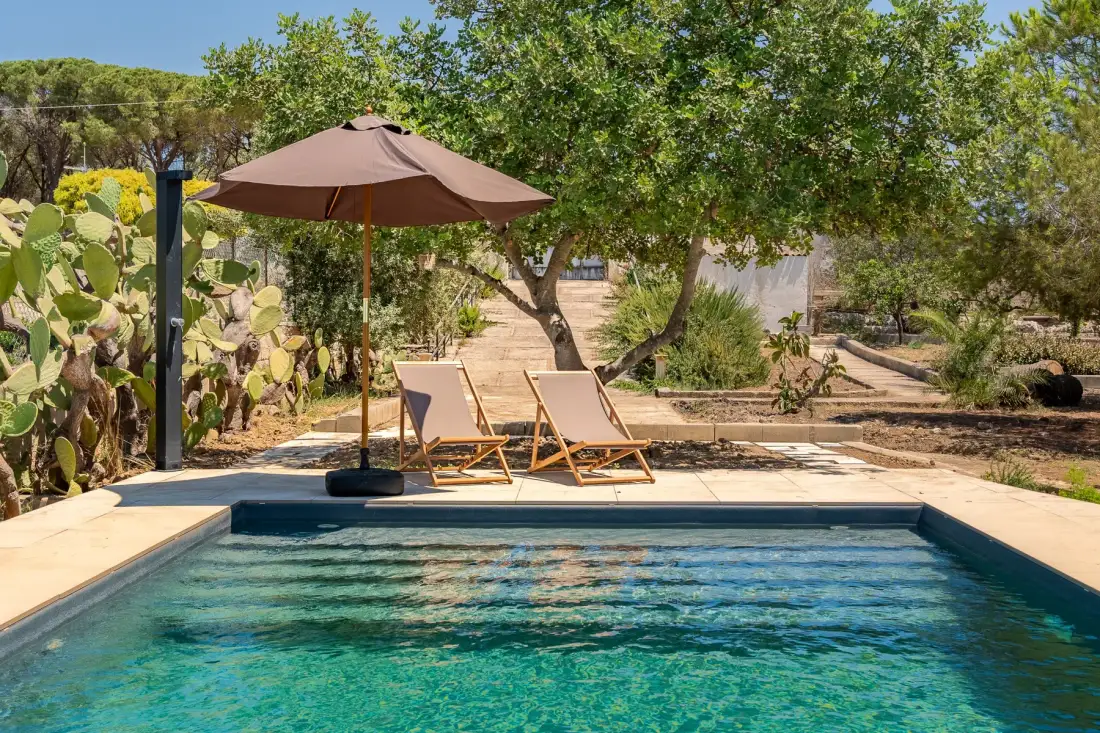 Una piscina está junto a dos tumbonas bajo una sombrilla.