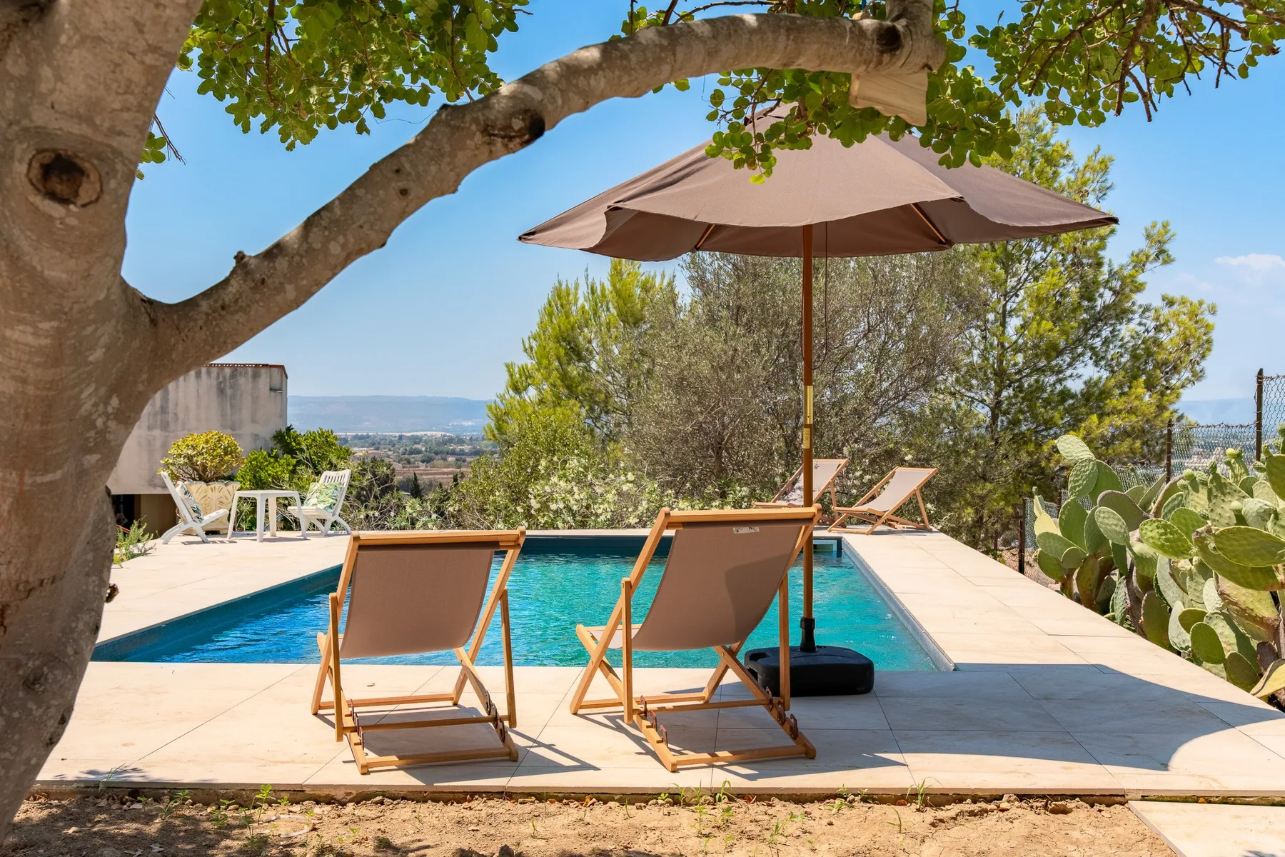 Una piscina al aire libre con tumbonas bajo una sombrilla grande.