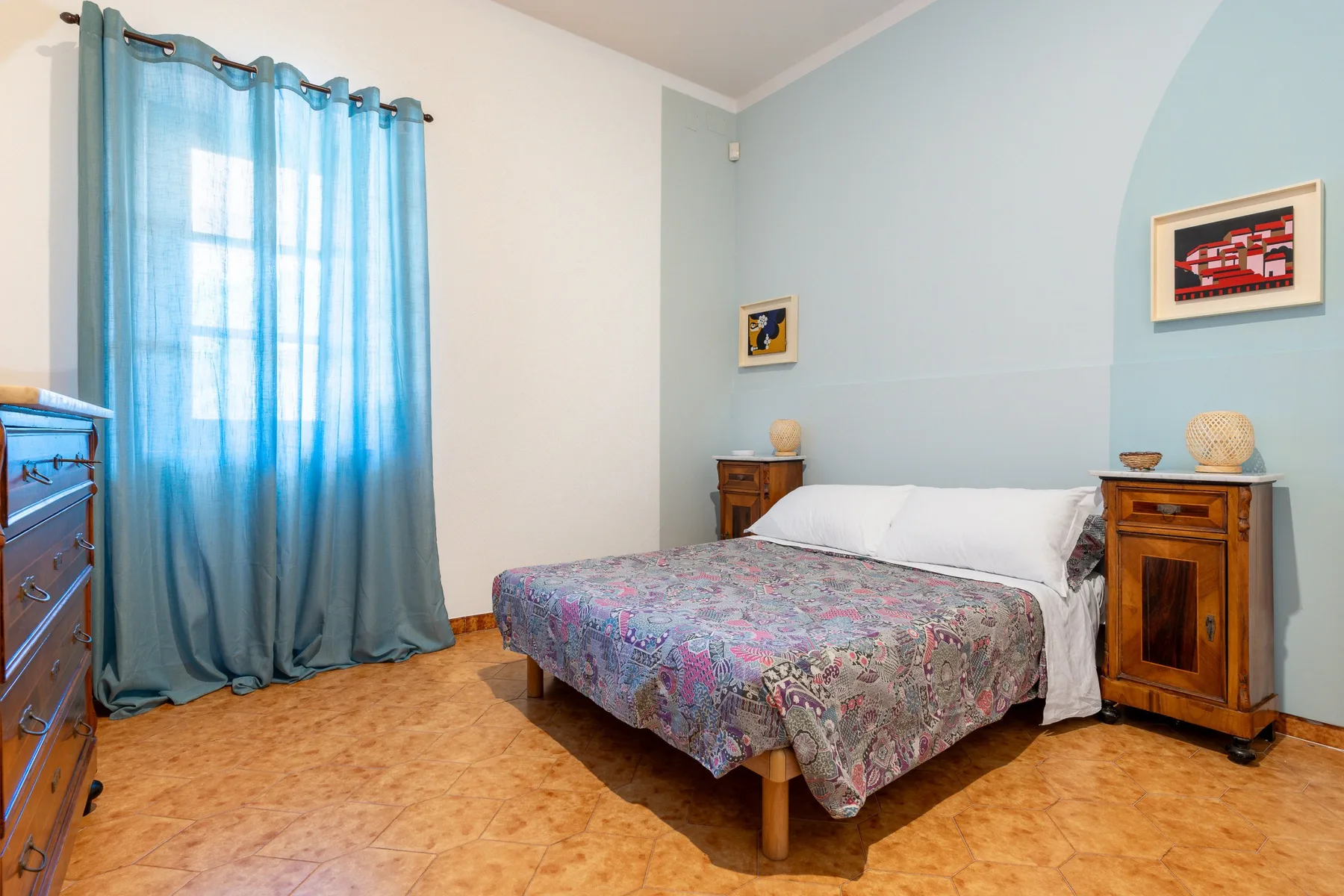 Un dormitorio con una cama, mesitas de madera y cortinas azules.