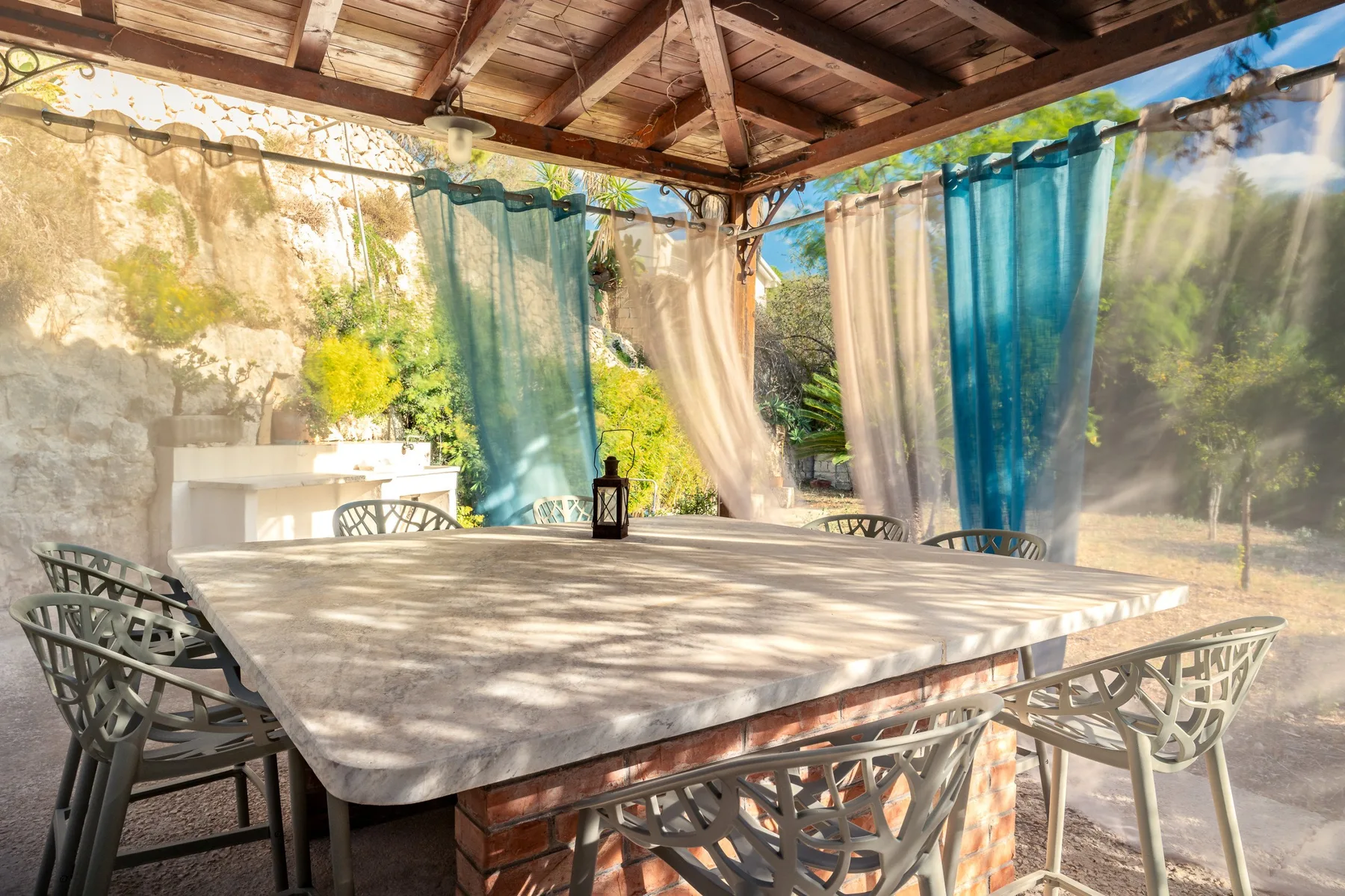 Comedor exterior cubierto con una mesa grande y cortinas translúcidas.